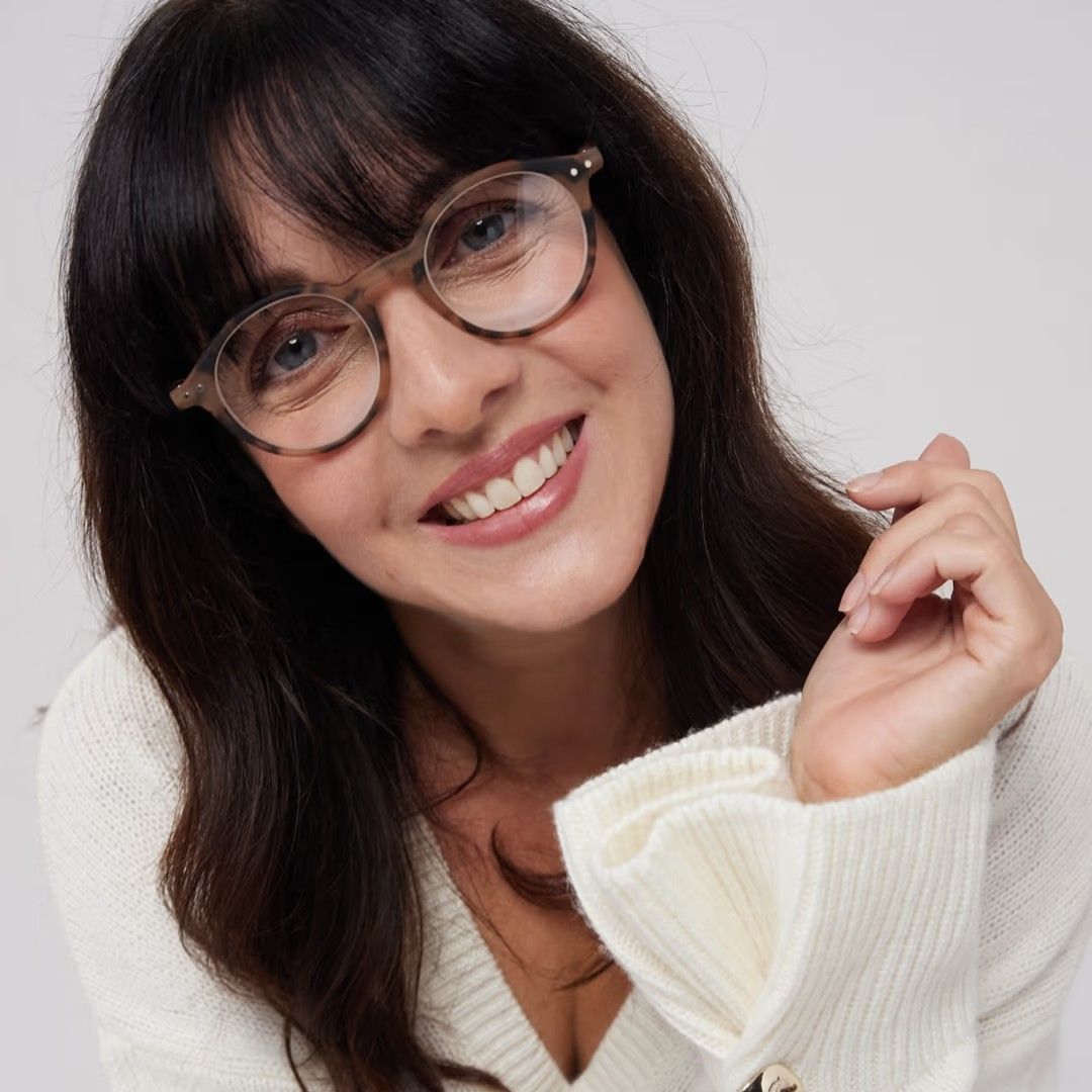 Woman wearing glasses and a white sweater against a plain background