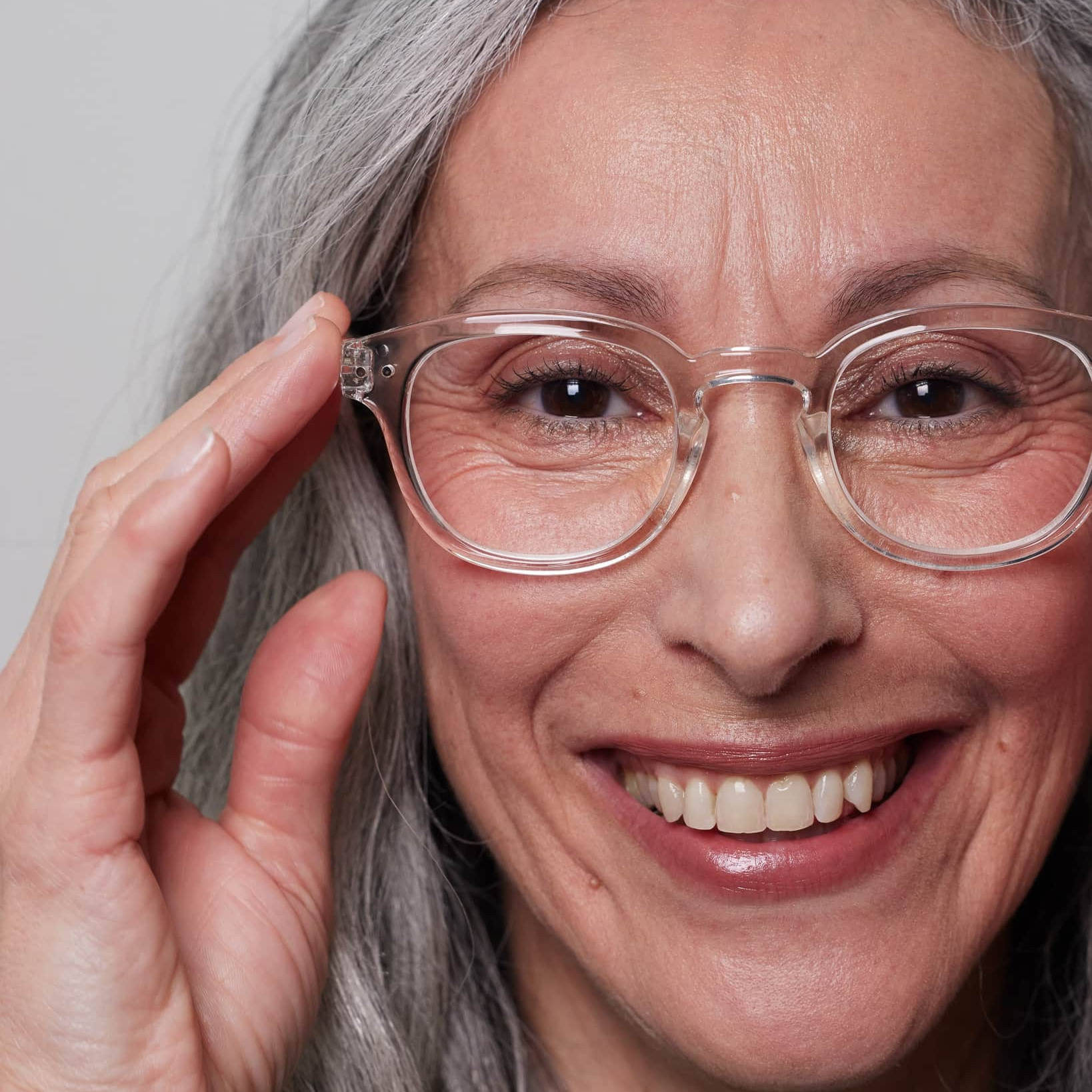 Woman with gray hair wearing glasses, adjusting them with a smile.