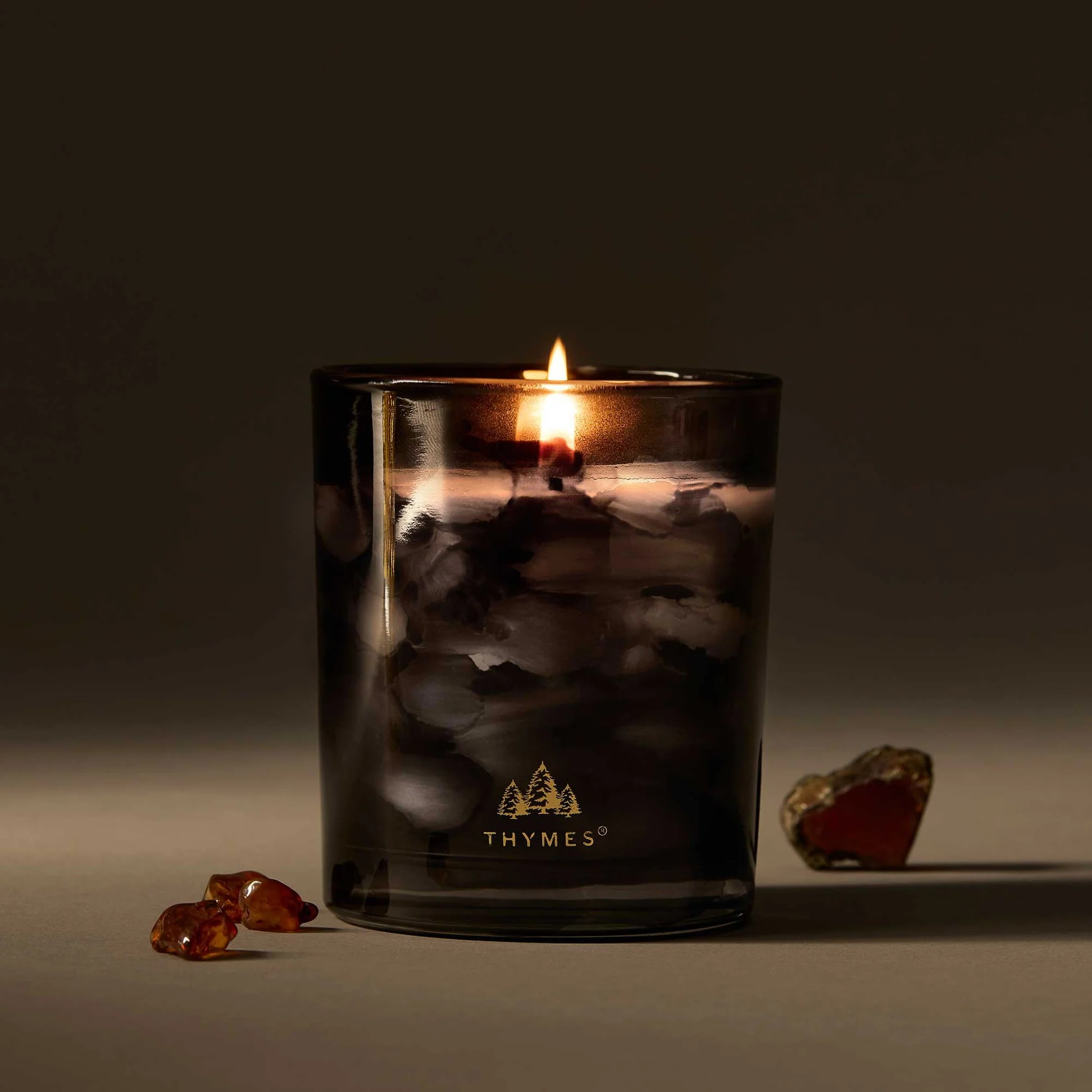 Thymes candle in a dark glass container with amber stones on a dark background