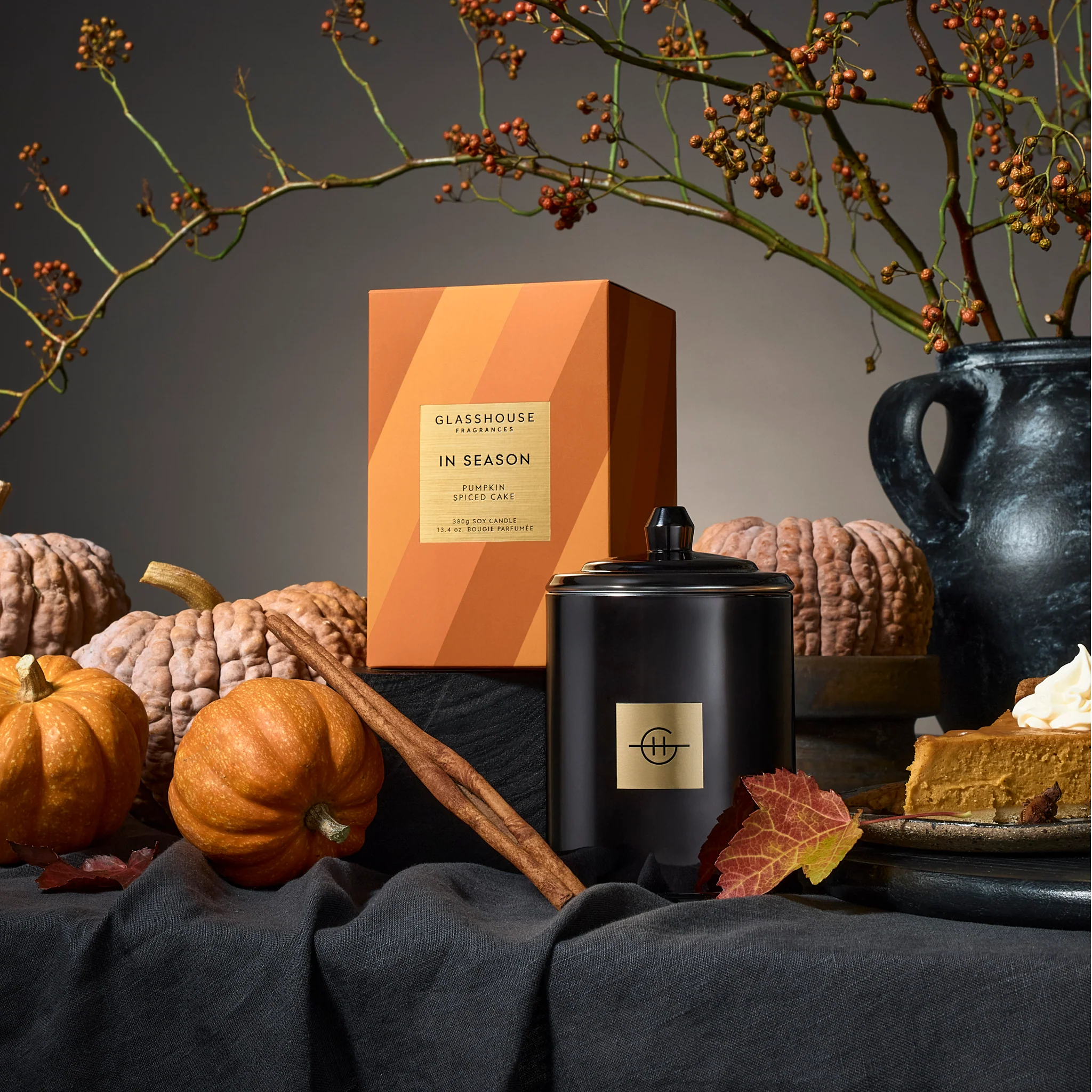 Glasshouse Candle Co candle with pumpkins, cinnamon stick, and decorative elements on a dark background.