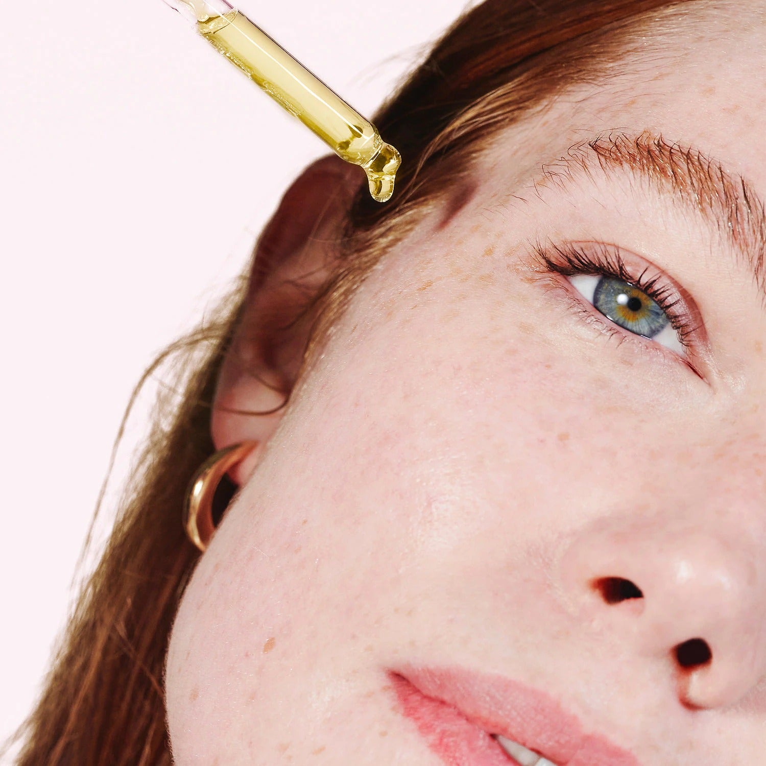 Close-up of a woman applying a gold-colored cosmetic product to her face with a dropper.