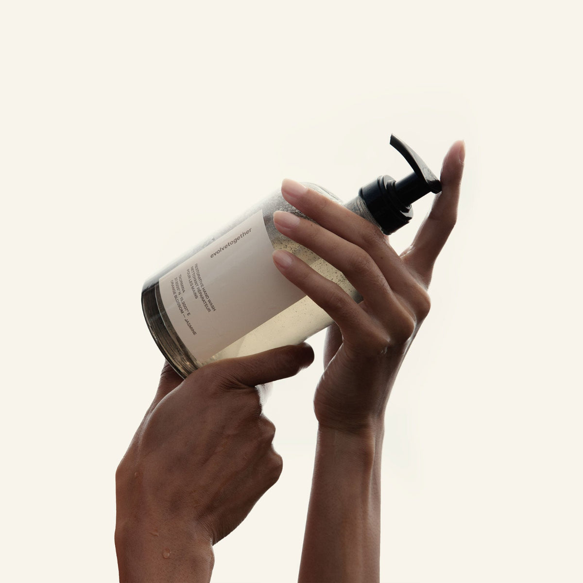 Person holding a bottle with a pump dispenser against a light background