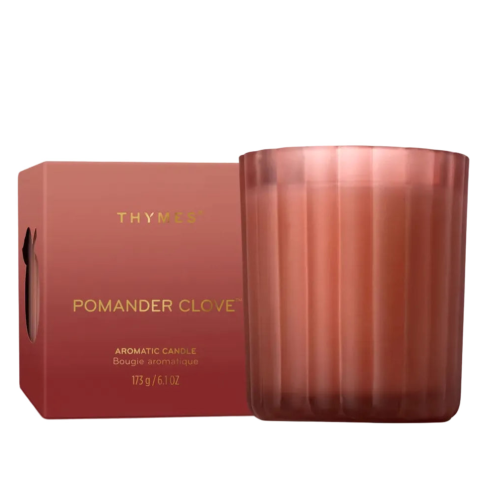 A Thymus Pomander Clove scented candle in a ribbed translucent rose-gold glass jar next to its matching rose-red cardboard box with gold lettering, set against a plain white background.
