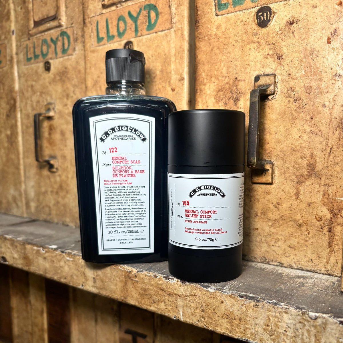 Two bottles of C. O. Bigelow products on a wooden surface with a vintage background.