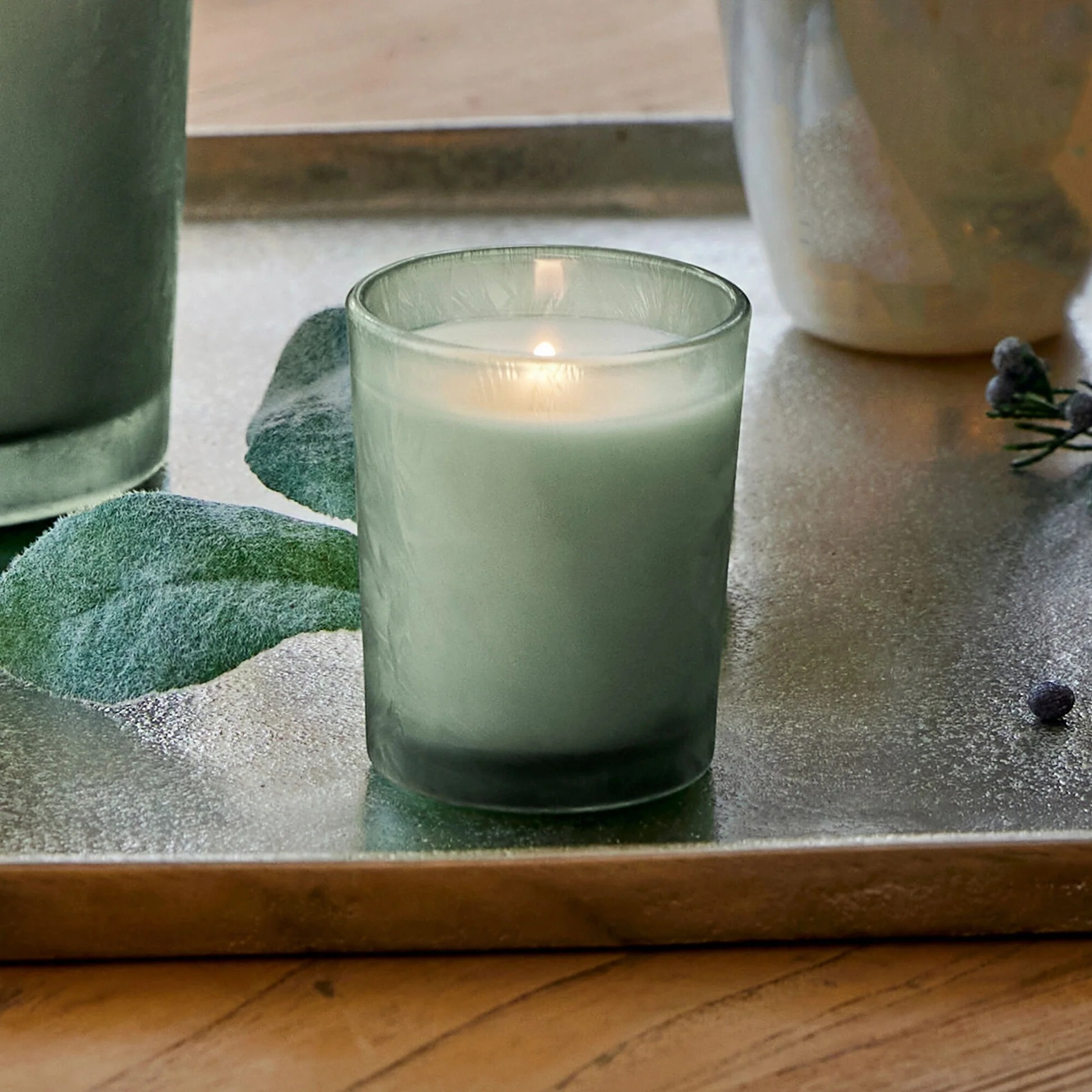 Green candle in a glass holder on a wooden surface with a blurred background