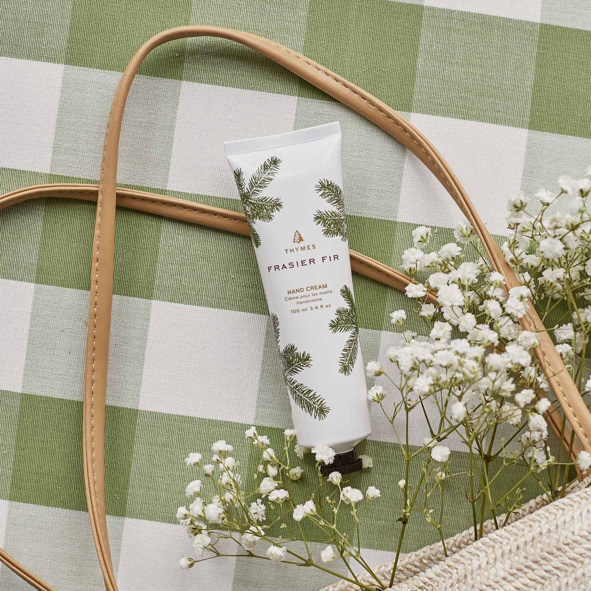 Hand cream tube with greenery design on a green checkered background with flowers