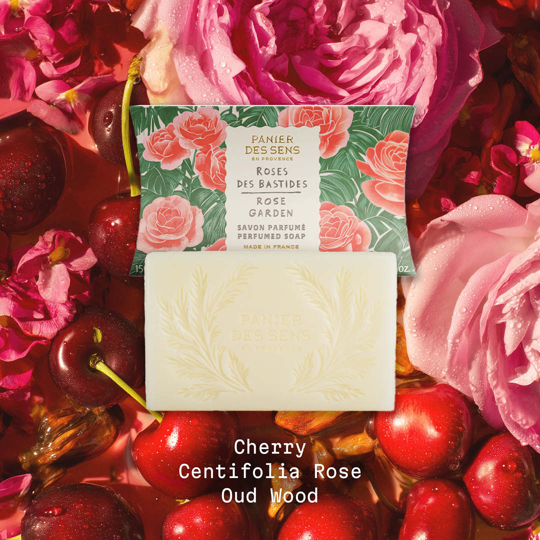 Panier Des Sens Bar of soap with floral and fruit-themed packaging on a bed of pink roses and cherries.