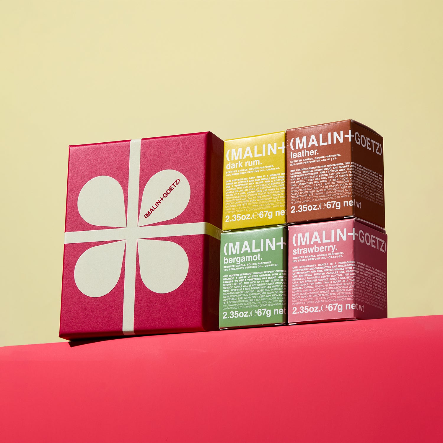 Five Malin+Goetz Scent the mood set with contents showing stacked on a red surface with a beige background