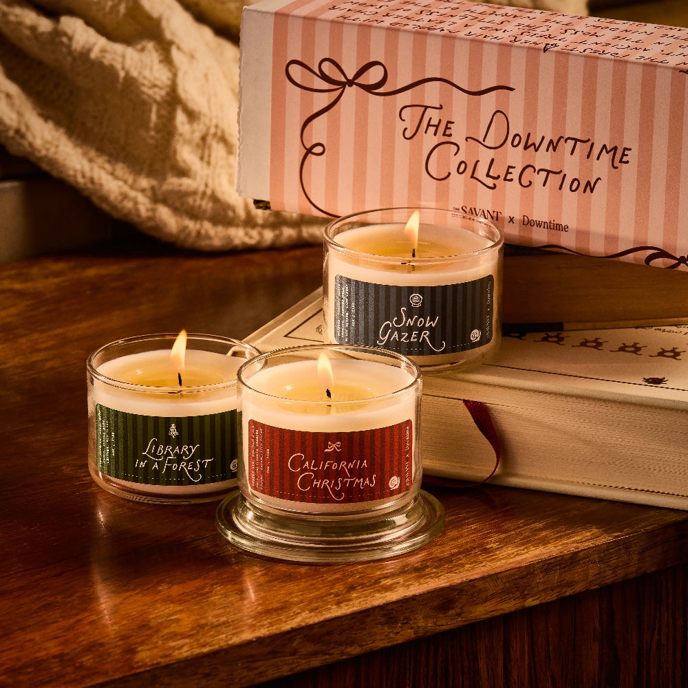 Three lit candles with labels on a wooden surface, next to a box labeled 'The Downtime Collection'.