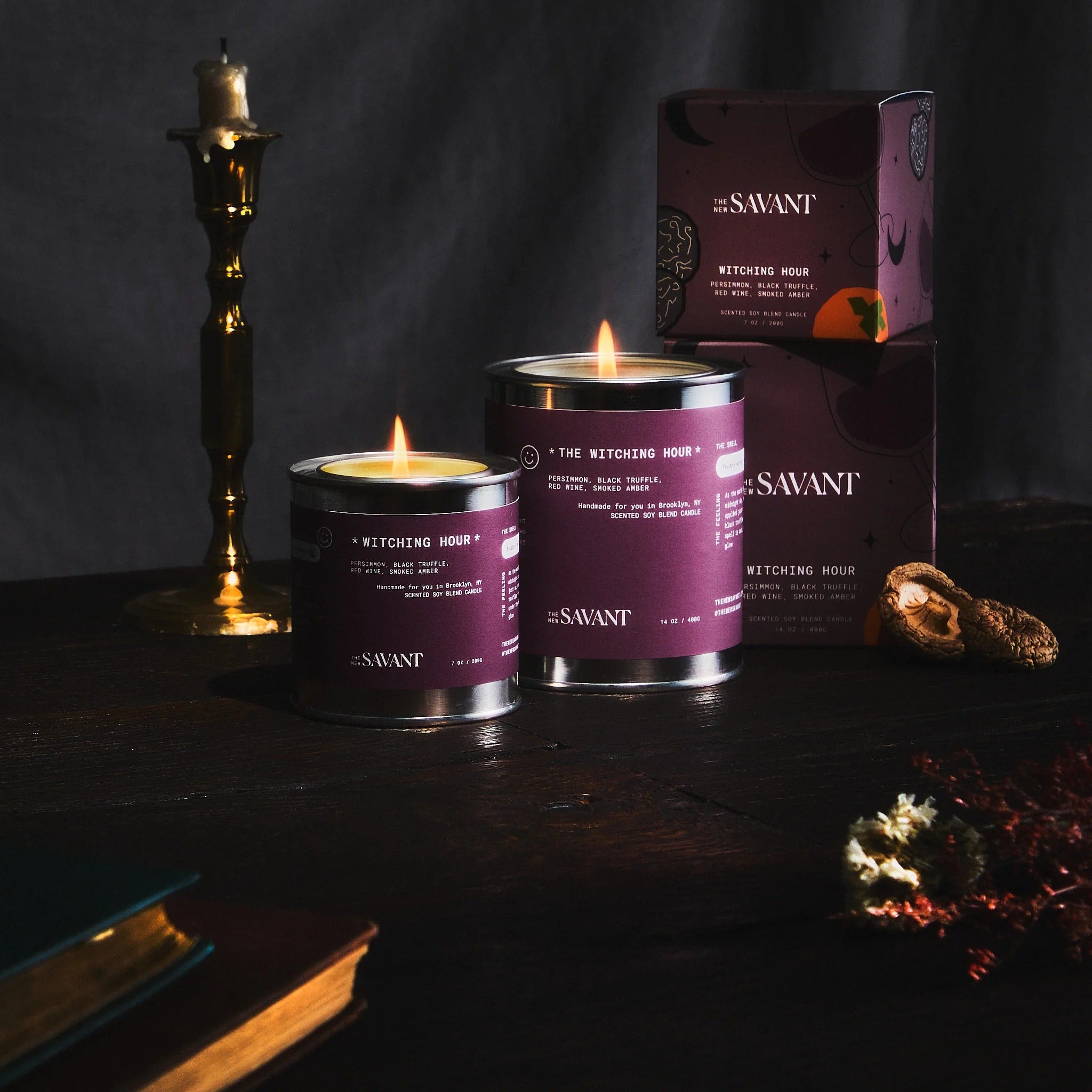 Two lit candles in purple tins with 'Savant' branding on a dark surface.