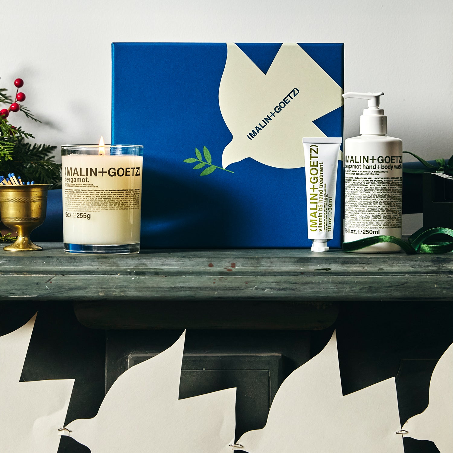 Malin+Goetz products including a candle, soap, and lotion on a wooden surface with a blue box in the background.