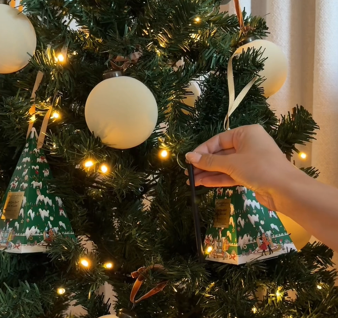 Hand decorating a Christmas tree with ornaments and lights