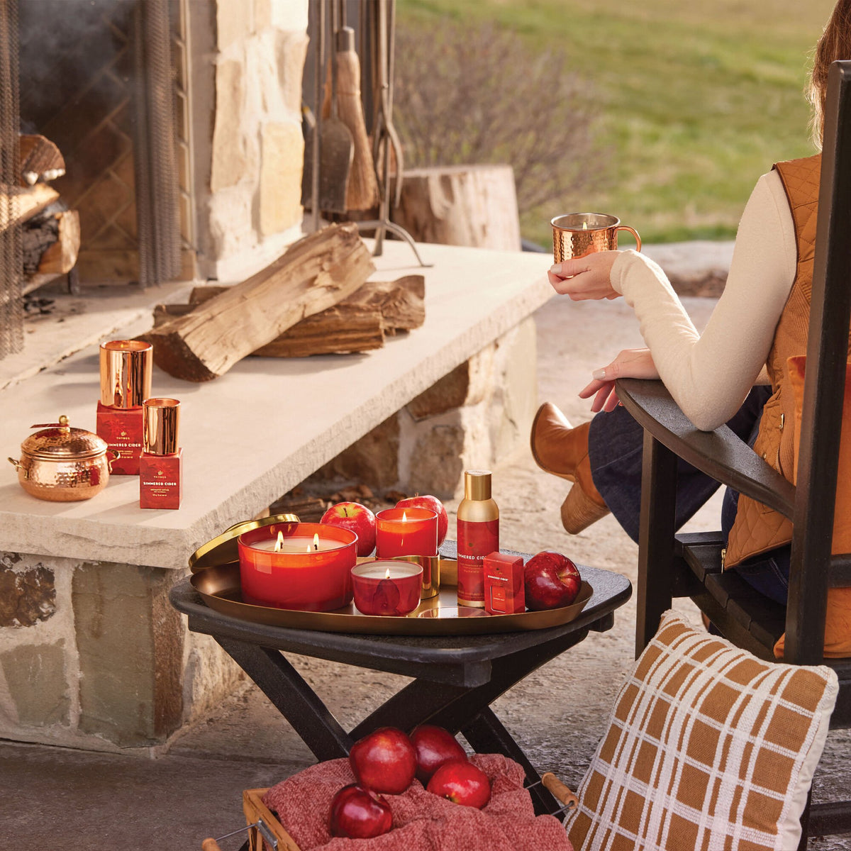 Person sitting by a stone fireplace with candles, apples, and decorative items.