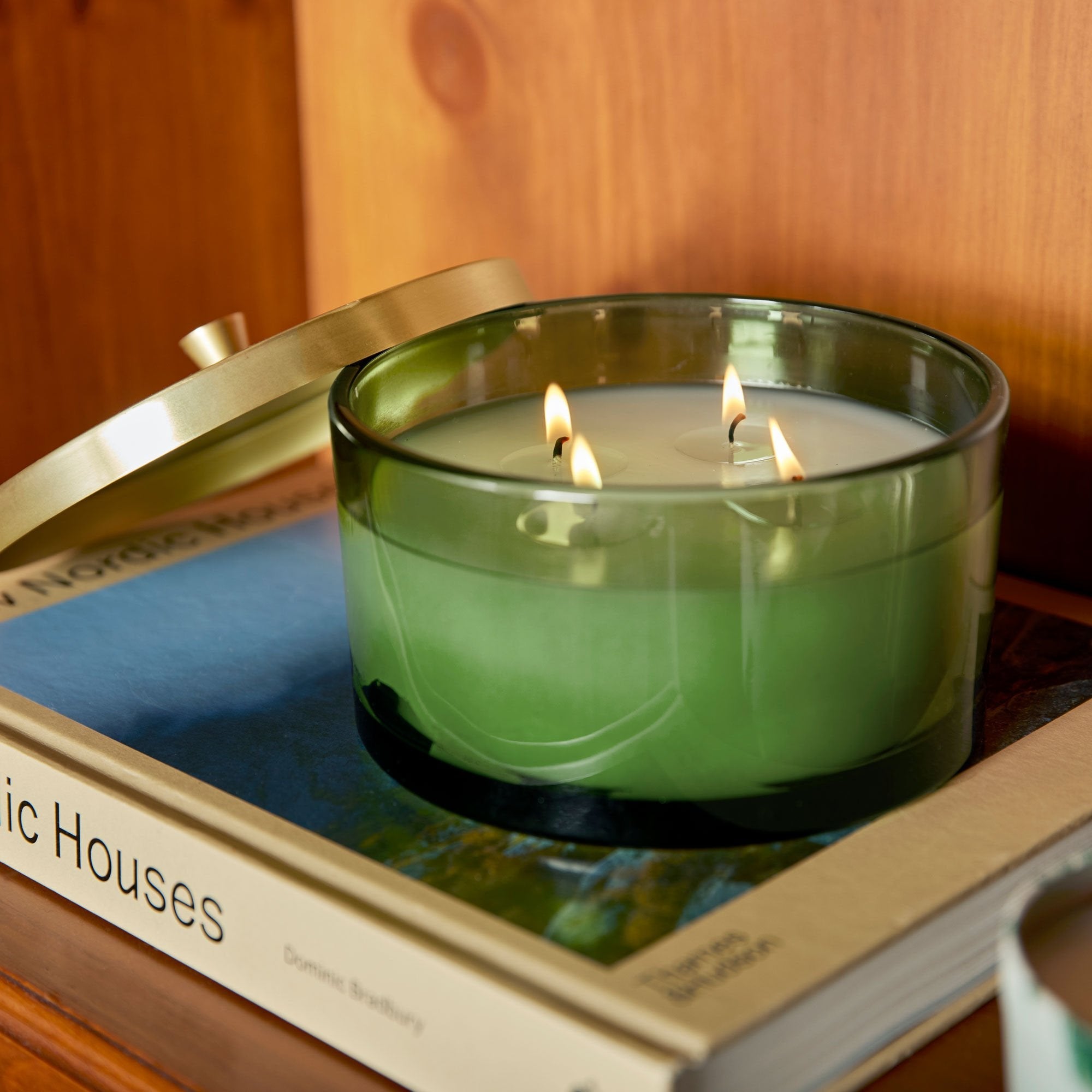 Green candle in a glass holder on top of a book with a wooden surface in the background