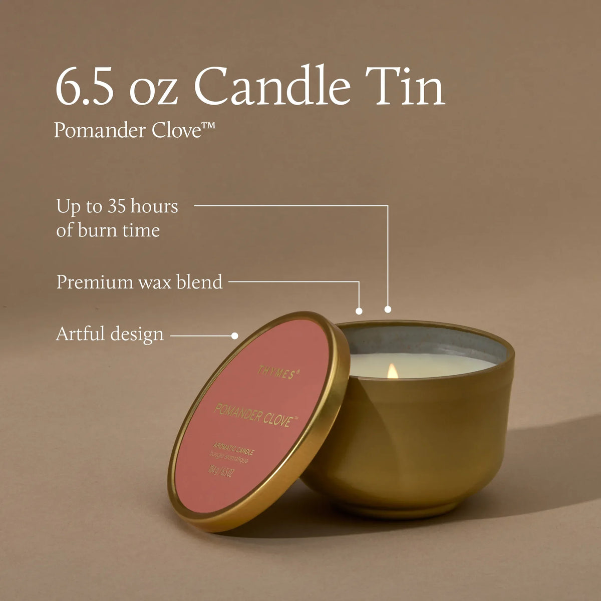 A 6.5 oz candle tin in a metallic gold finish with a pink lid, shown on a warm taupe background with text callouts about burn time, wax blend, and artful design.