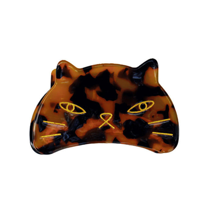 A clip in the shape of a cat's head with a etched gold pattern.