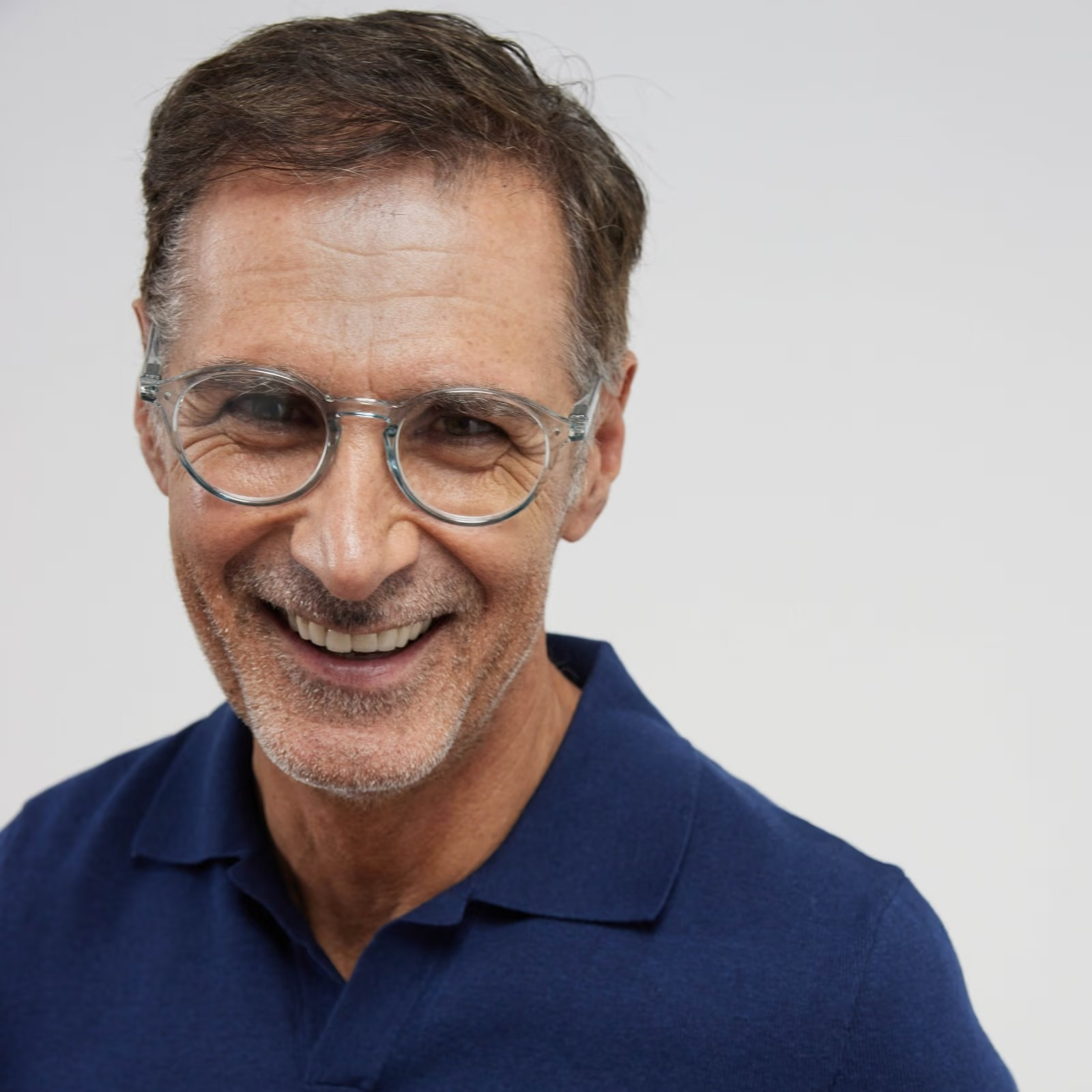 Man wearing glasses and a blue polo shirt on a plain background