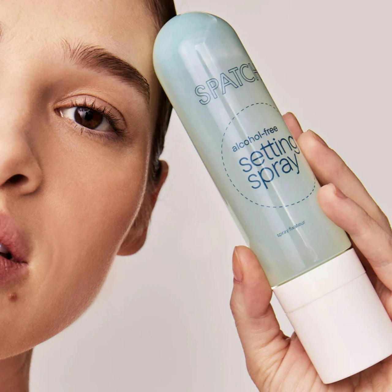 Person holding a SPATCHCO setting spray can near their face on a plain background