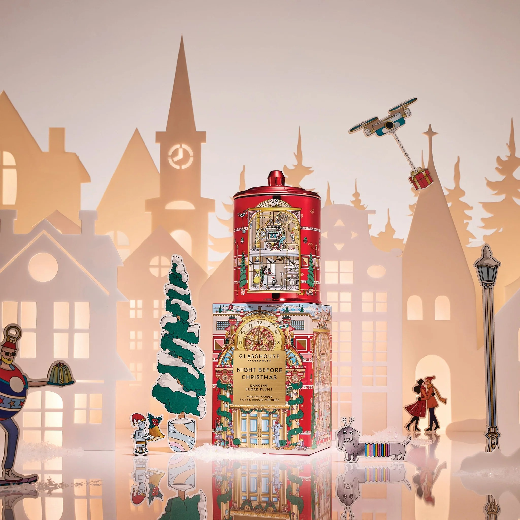 Decorative Christmas scene with a tall red and gold tower, trees, and people against a snowy village backdrop.