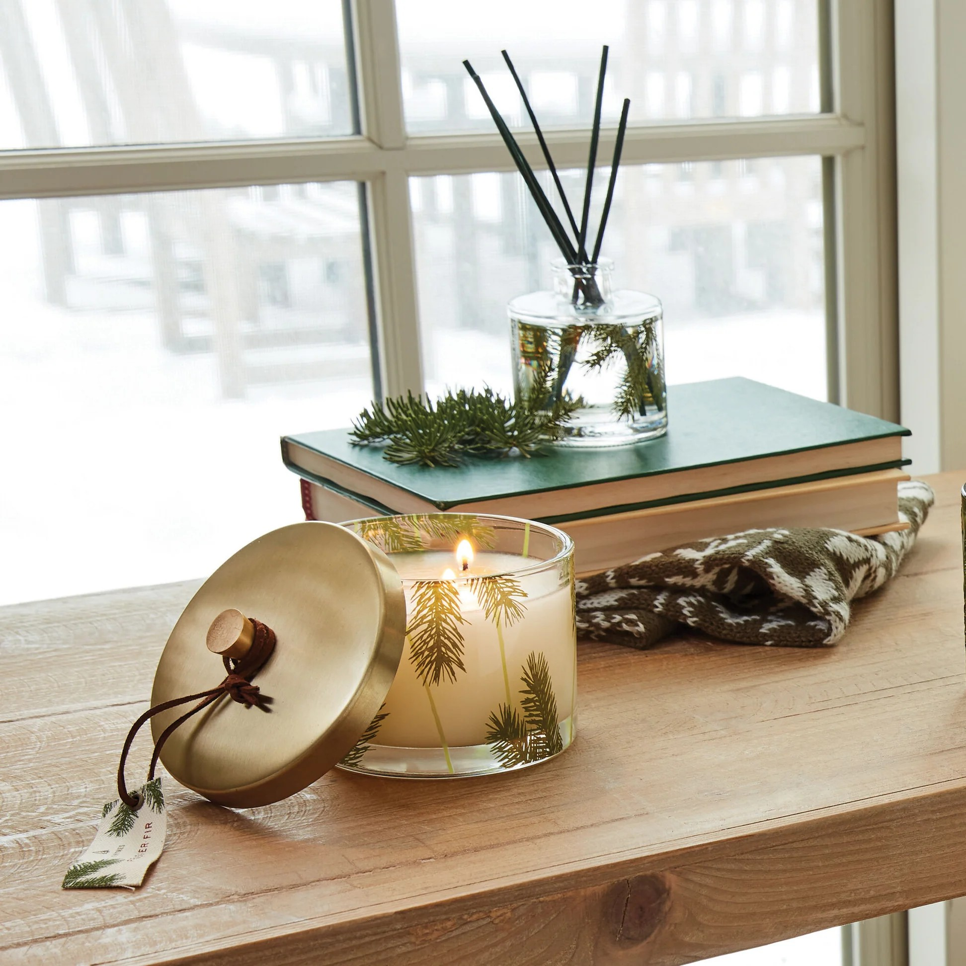 Candle with a gold lid on a wooden surface with a window in the background