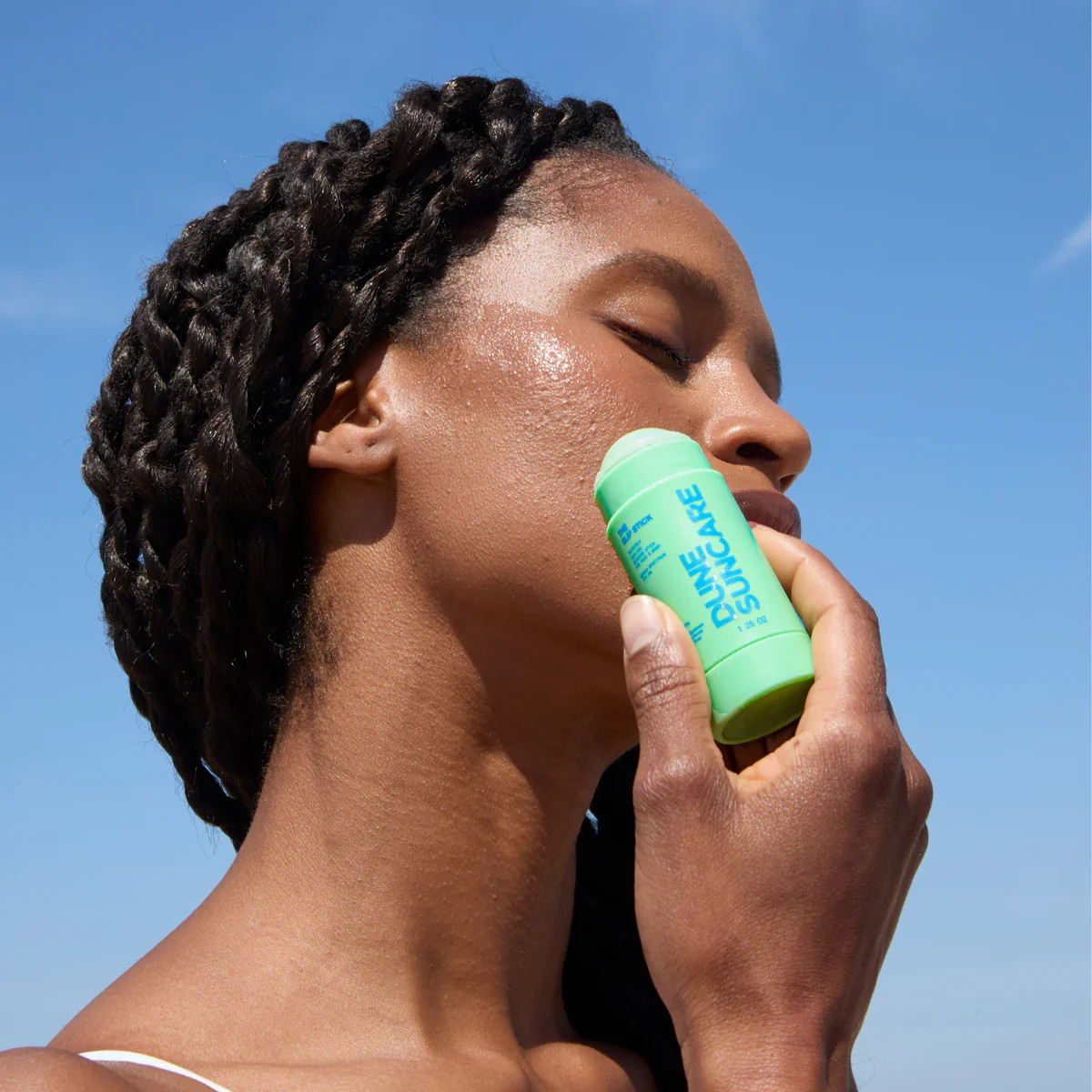 Person applying sunscreen stick with clear blue sky background