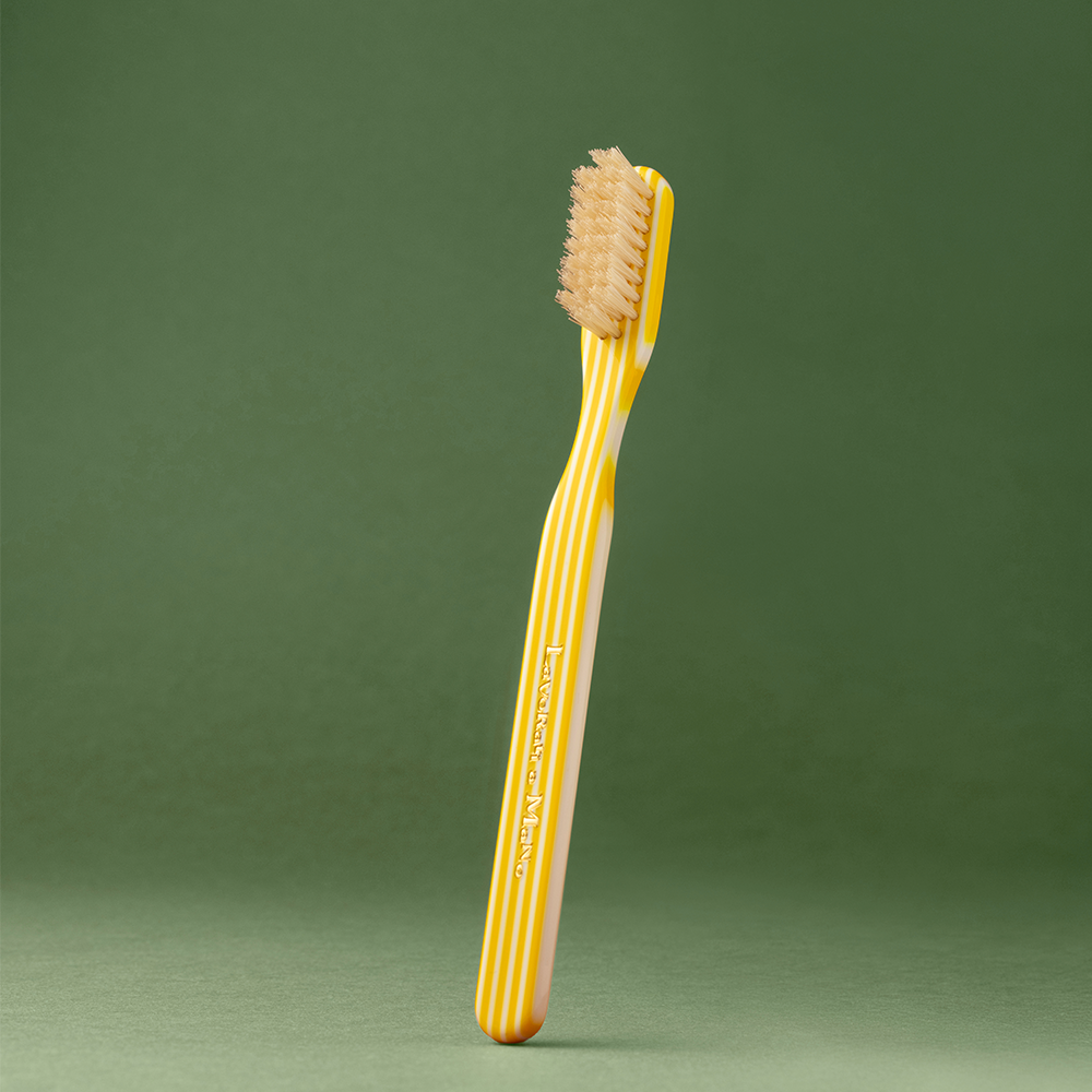 A single toothbrush with a yellow and white striped handle and beige bristles, standing upright against a solid dark green background.